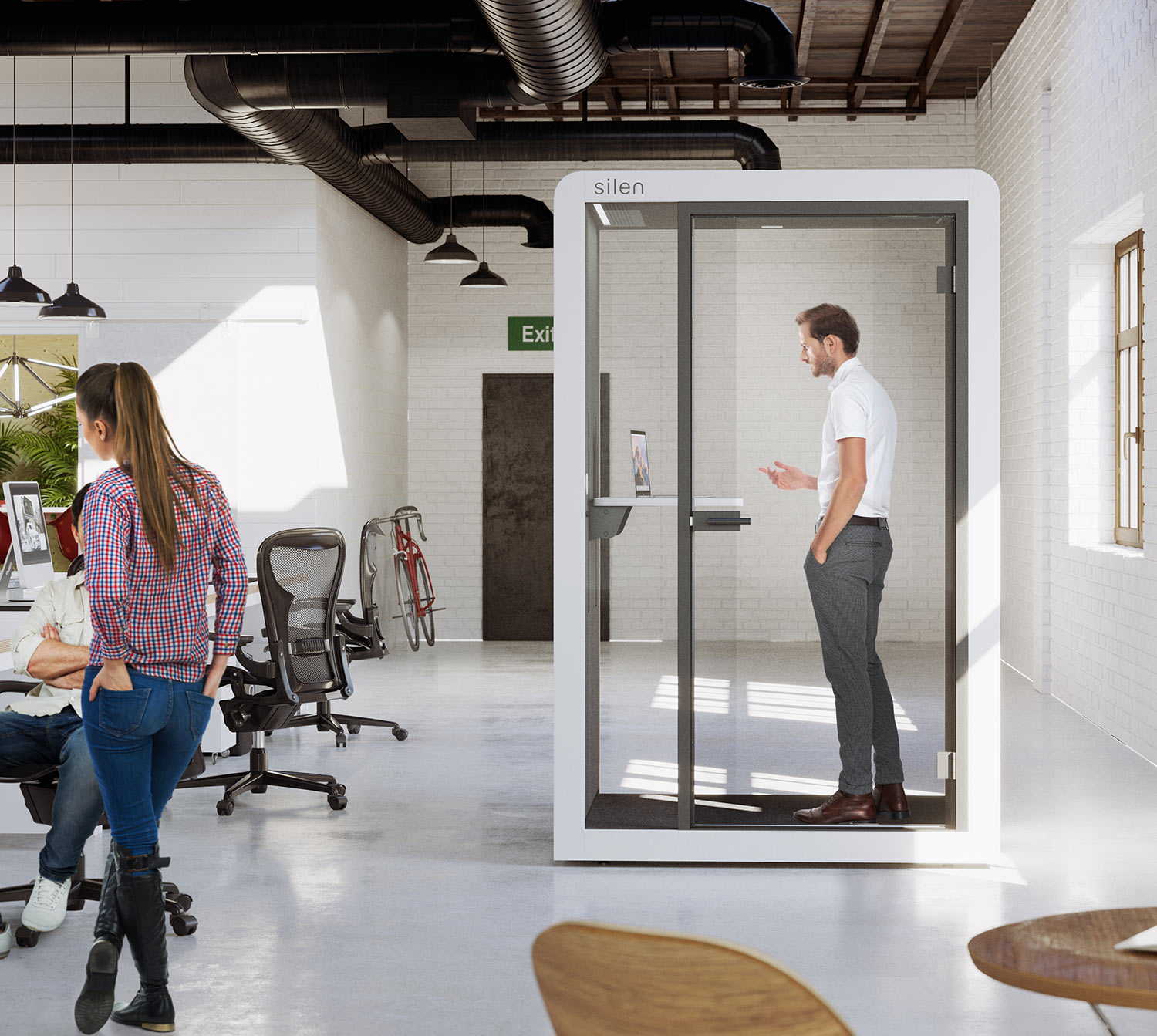 man standing in a Silen space 1.5 booth having a videocall inside and open office