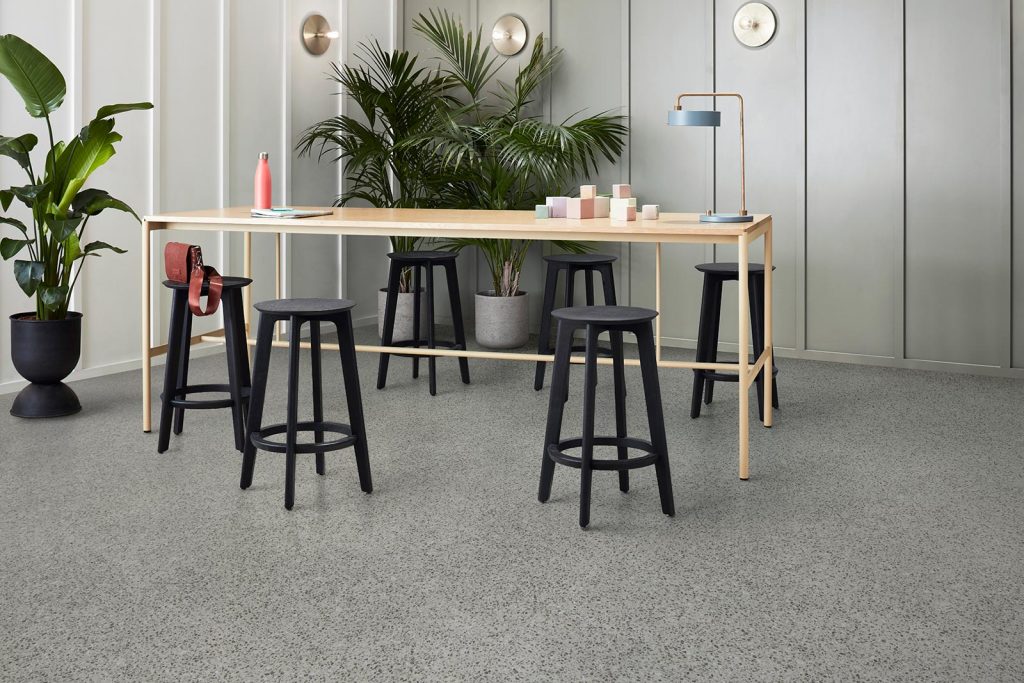 high table with stools around it and big planters with plants against the walls. On the floor there is in the mix lvt for authentic terrazzo look